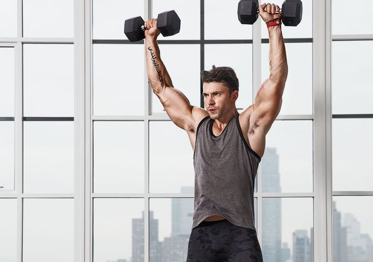 Man performing a standing shoulder press with dumbbells.