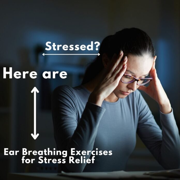 A stressed woman holding her head with both hands, sitting in a dimly lit room. Text overlay reads: 'Stressed? Here are Ear Breathing Exercises for Stress Relief.' Image illustrating stress relief techniques through ear breathing exercises.